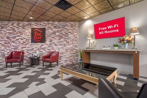 A Red Roof Inn lobby with a checkered floor, two red armchairs, a coffee table, a fireplace, and a sign indicating free Wi-Fi in all rooms.