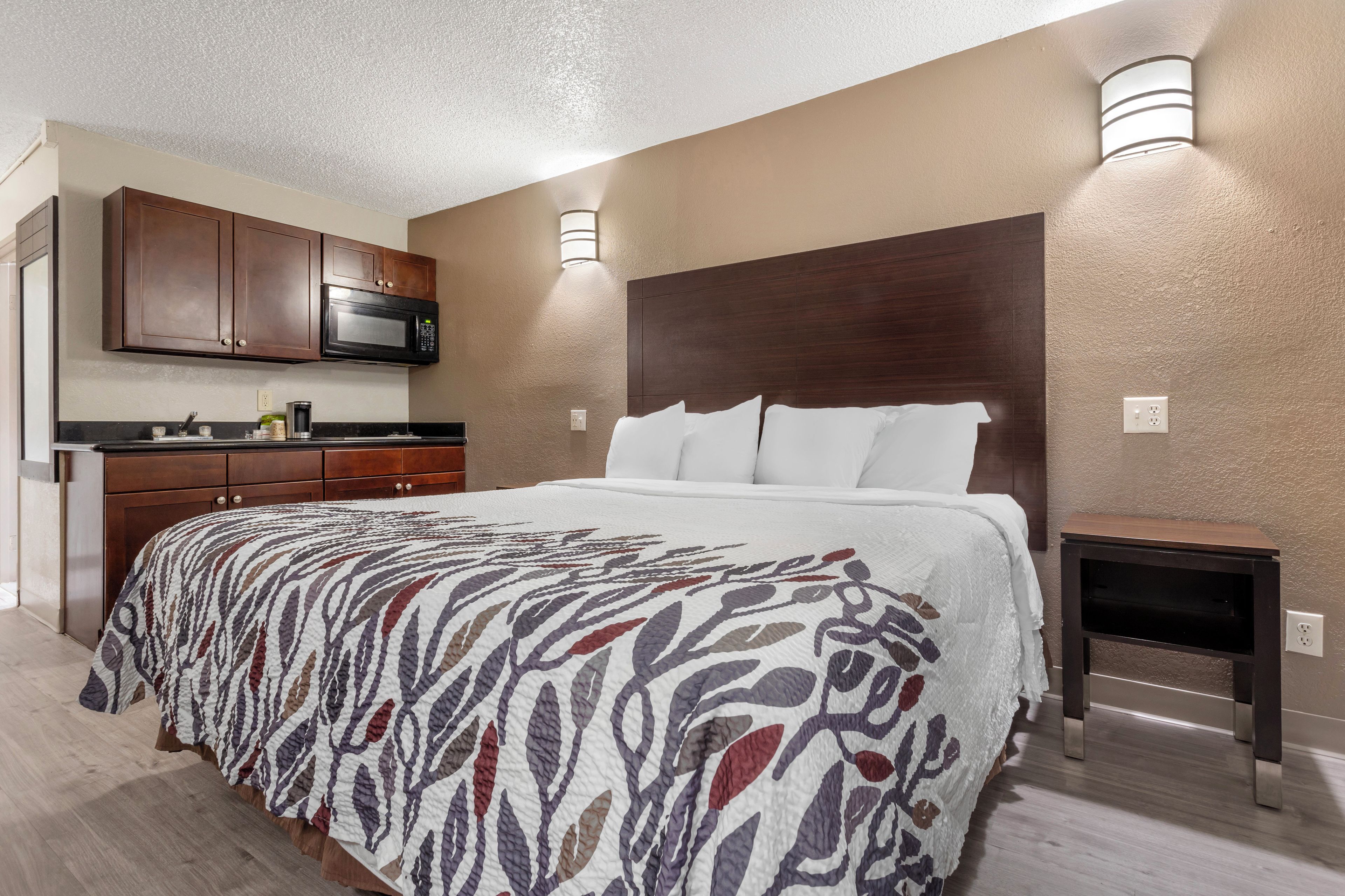 Una habitación de hotel con una cama, una mesita de noche, un microondas, una cafetera y una pequeña mesa.