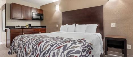 Una habitación de hotel con una cama, una mesita de noche, un microondas, una cafetera y una pequeña mesa.