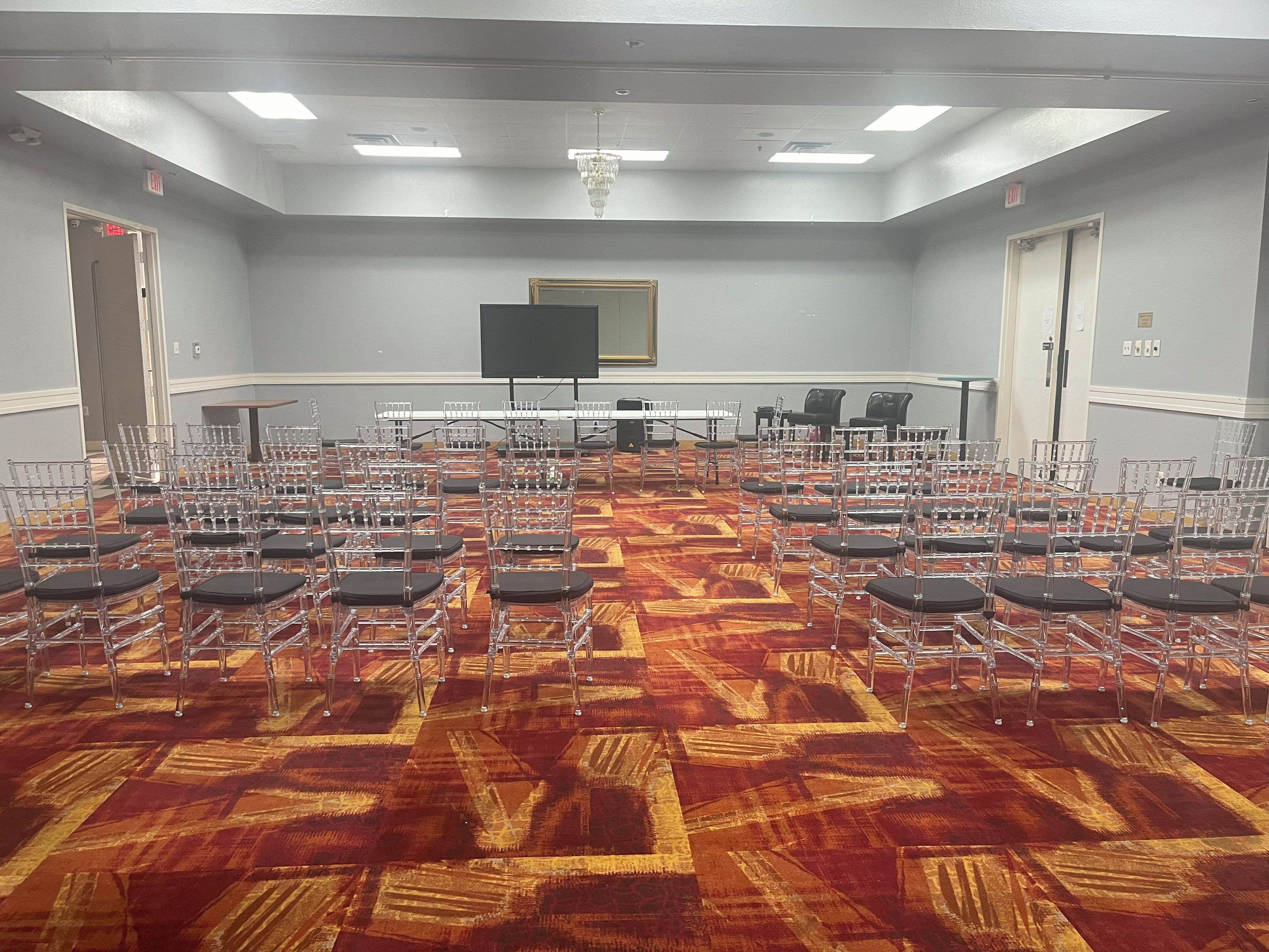 A conference room with rows of chairs, a large screen, and a patterned carpet.
