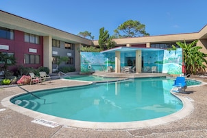 A swimming pool with a tropical mural, surrounded by lounge chairs and a building with multiple windows.