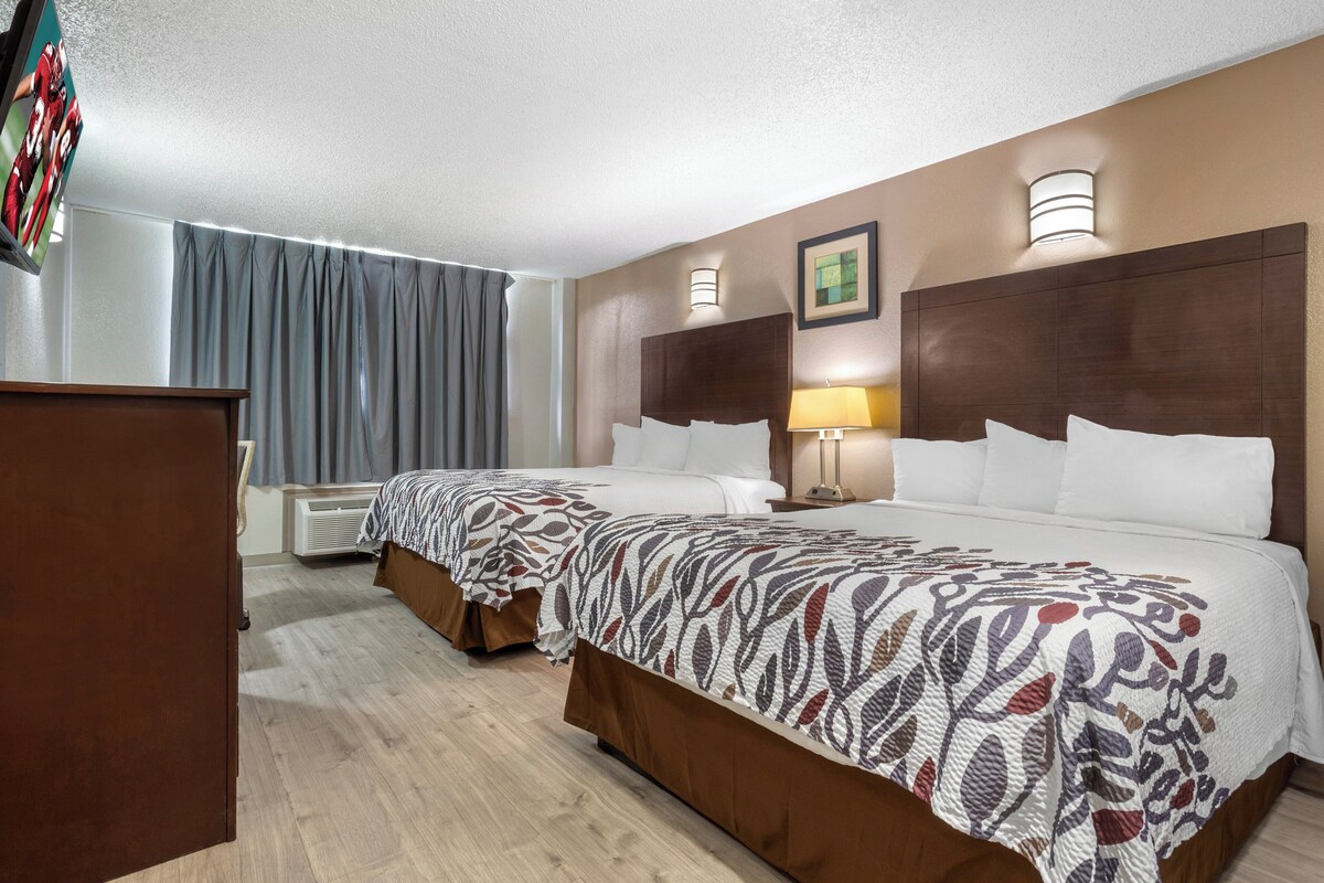 A hotel room with two beds, a wooden wardrobe, a flat-screen TV, a wall-mounted lamp, and a framed picture.