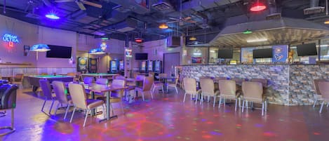 A bar area with pool tables, chairs, and a stone wall bar counter.