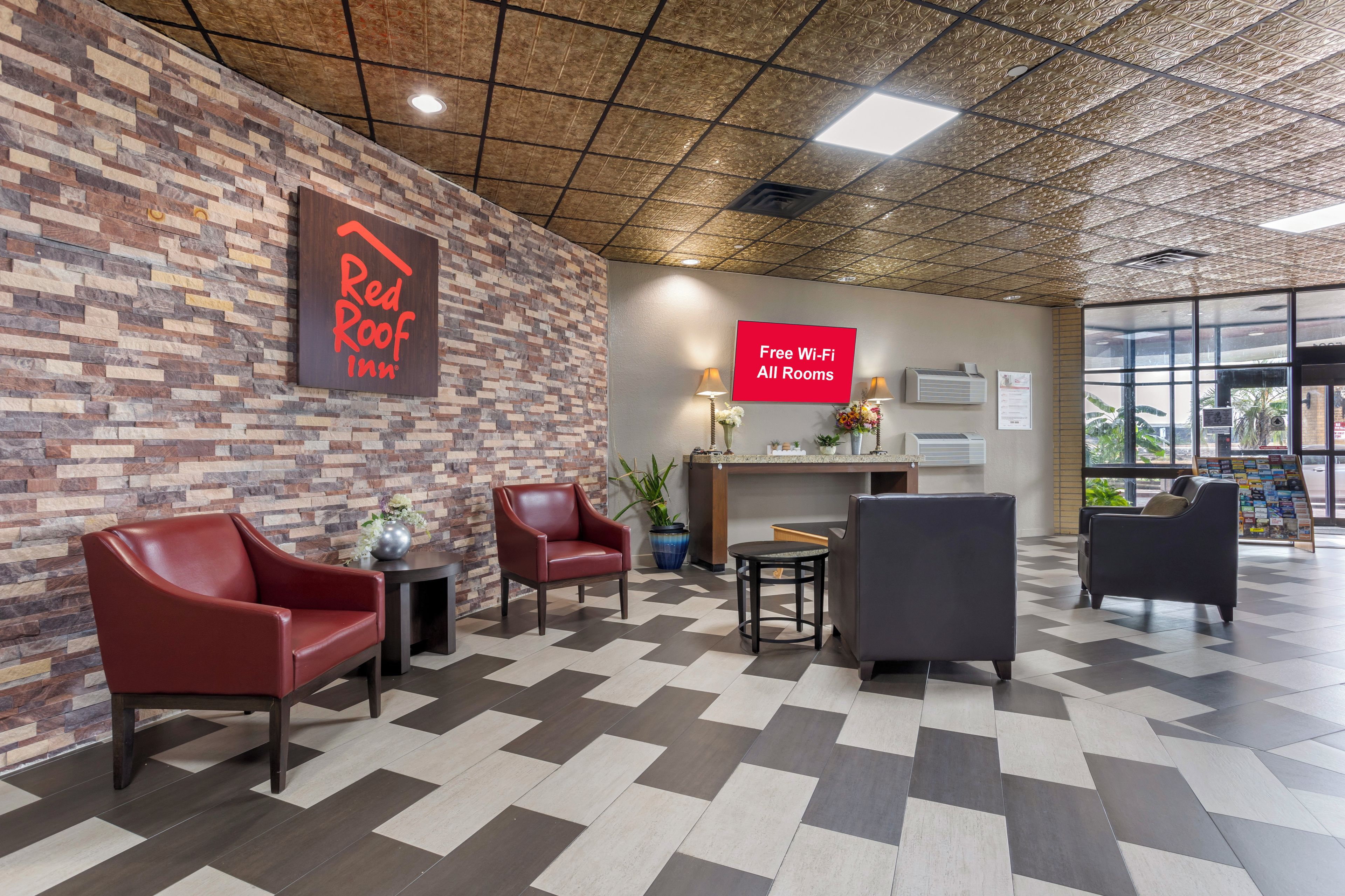 Een receptie van Red Roof Inn met een zwart-wit geruit vloertje, lederen zitplaatsen en een bordje dat gratis Wi-Fi in alle kamers aangeeft.