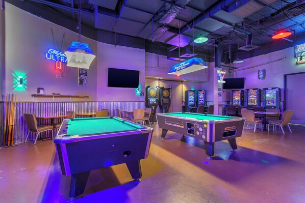 A pool table area with neon signs, a billiards table, and arcade machines. - Red Roof Inn La Marque (La Marque)