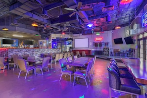 An indoor bar with tables and chairs, a stage, and a screen. - Red Roof Inn La Marque– Texas City (La Marque)