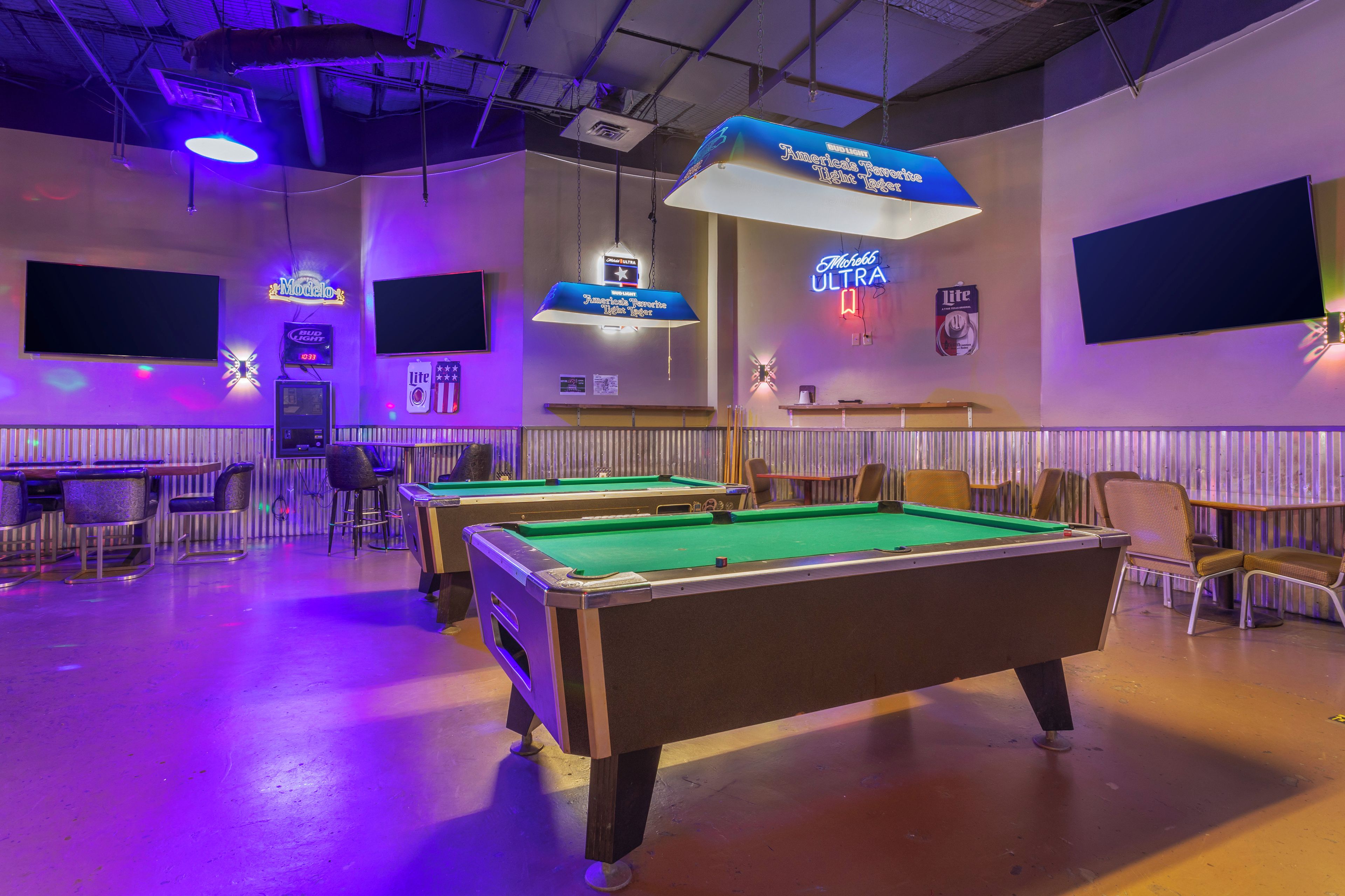 A billiards room with two pool tables, chairs, and neon signs advertising Bud Light and Michelob Ultra.