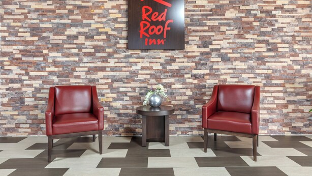 Une enseigne « Red Roof Inn » sur un mur à texture, deux fauteuils en cuir et une petite table avec un vase.