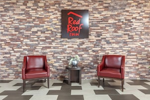 A Red Roof Inn sign on a textured wall, two leather chairs, and a small table with a vase.