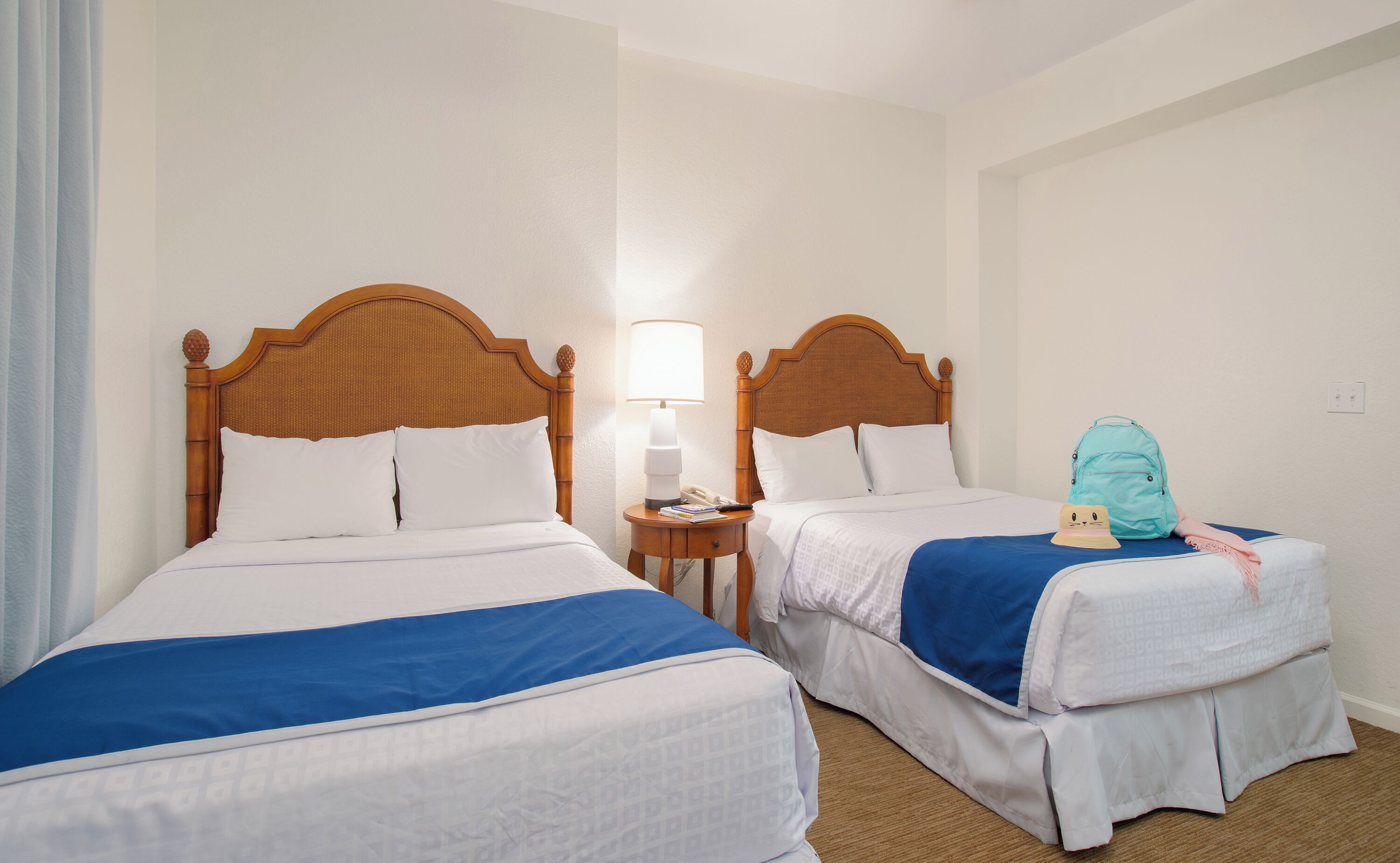 Two single beds with wooden headboards, a bedside table with a lamp, and a backpack on the floor.