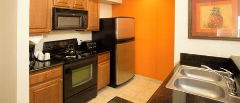 A compact kitchen with wooden cabinets, a microwave, a stove, a refrigerator, and a sink.