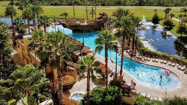 A resort with multiple swimming pools, a pirate ship-themed water attraction, and lush greenery.