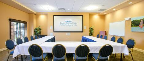 Una sala de conferencias con una mesa larga, sillas, una pantalla de proyector y una pizarra.