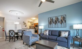 Uma sala de estar com um sofá azul, uma poltrona estampada e uma mesa de centro.