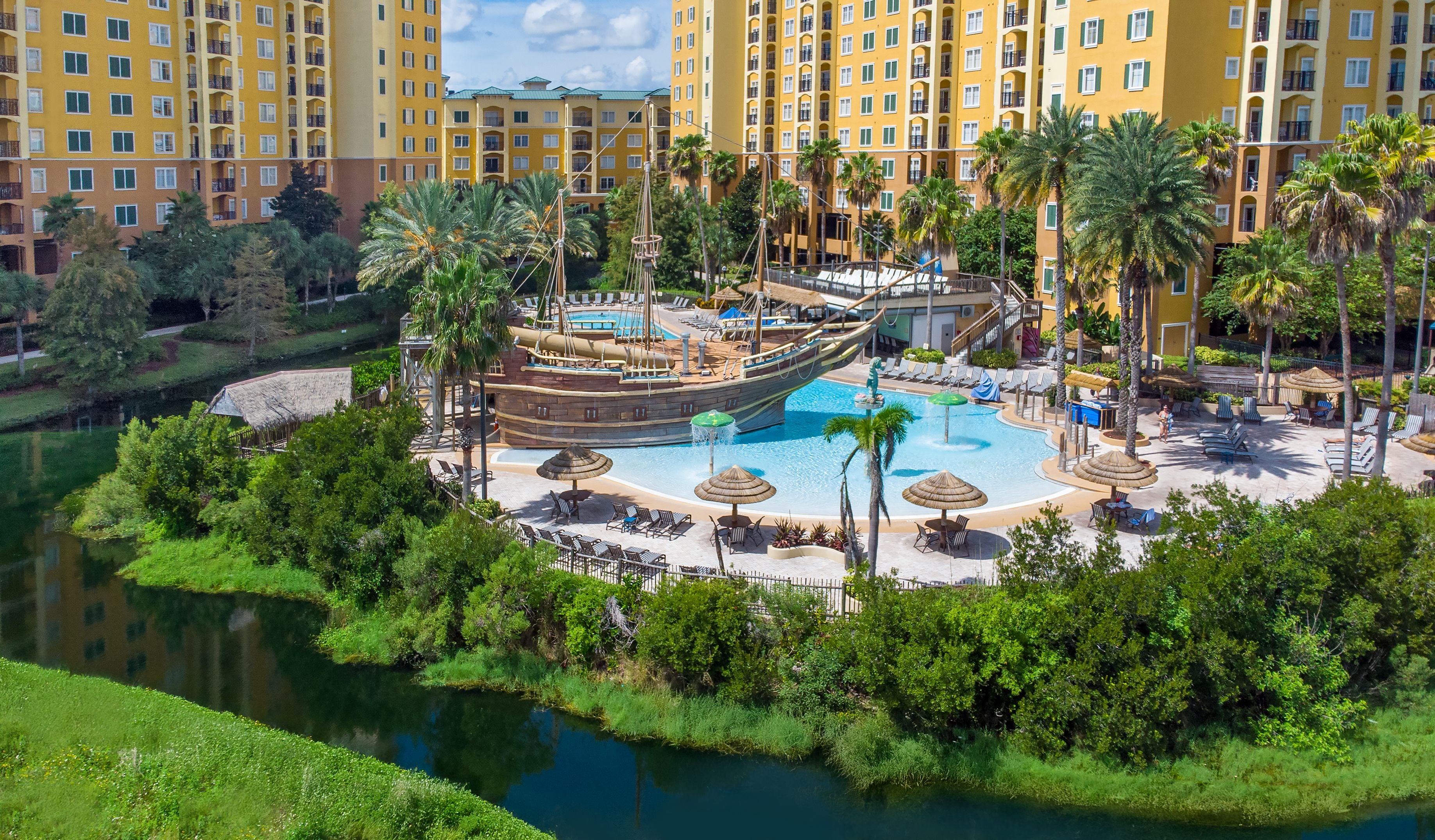 A resort with a large pool, palm trees, and a ship-shaped water feature.