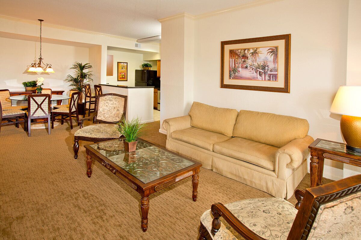 A living room with a beige sofa, wooden chairs, a glass coffee table, and a dining area with a round table and chairs.