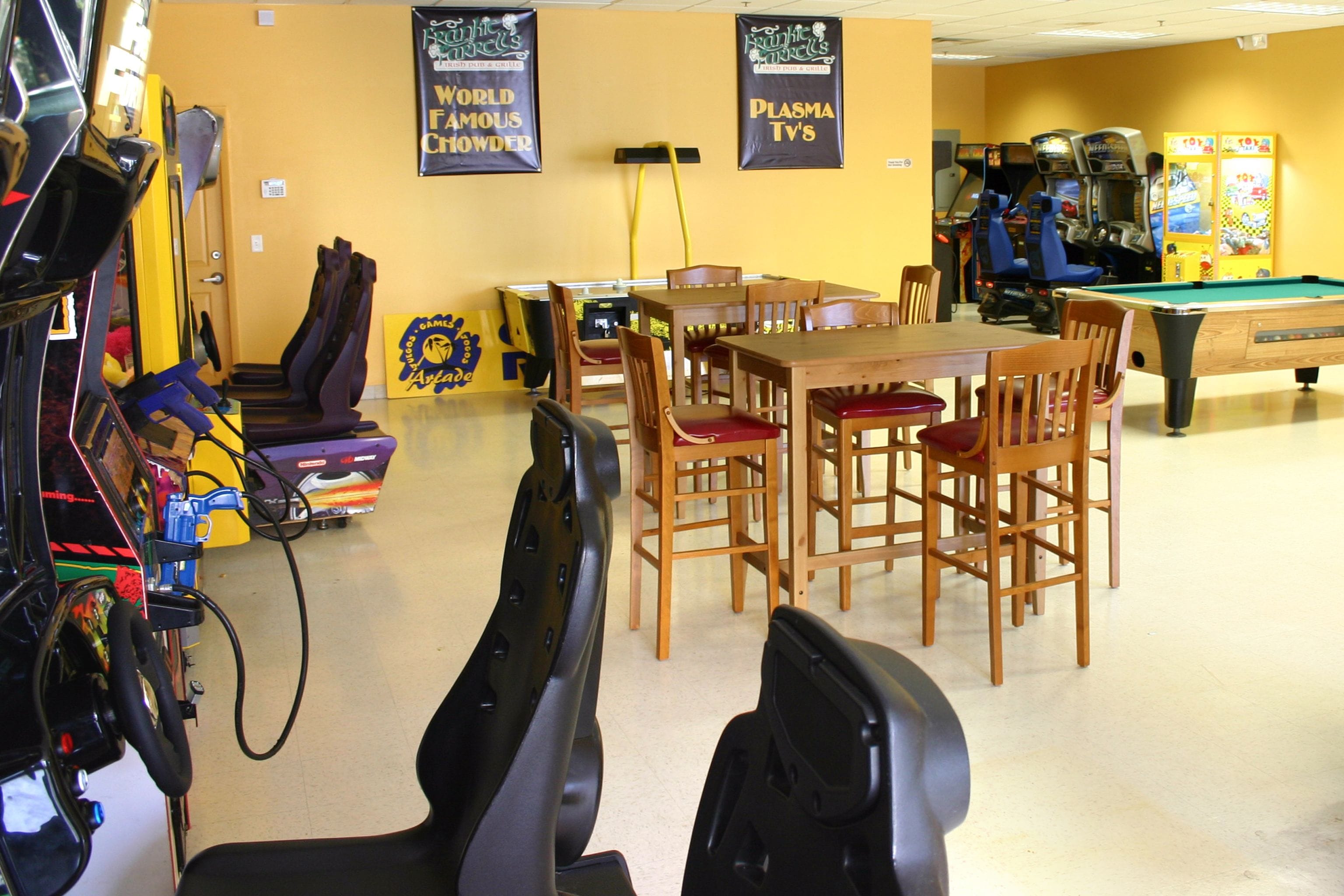 A room with a pool table, arcade machines, and a dining area with wooden chairs and a table.
