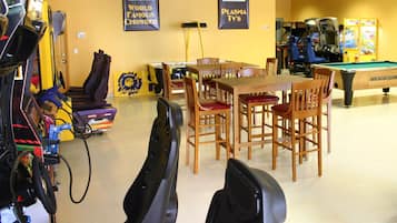 A room with a pool table, arcade machines, and a dining area with wooden chairs and a table.
