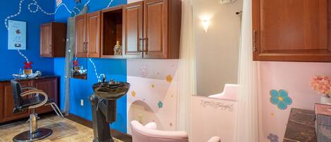 Un baño con pared azul, armarios de madera, una silla rosa y un espejo.