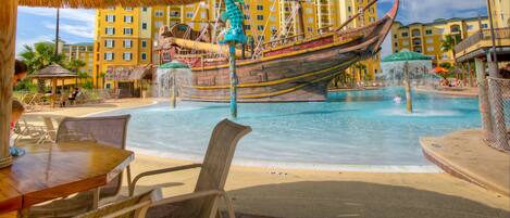 Una piscina con una fuente en forma de barco, sillas de descanso y un paraguas de paja.