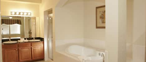 A bathroom with a large bathtub, a vanity with a mirror and lights, and a shower area.
