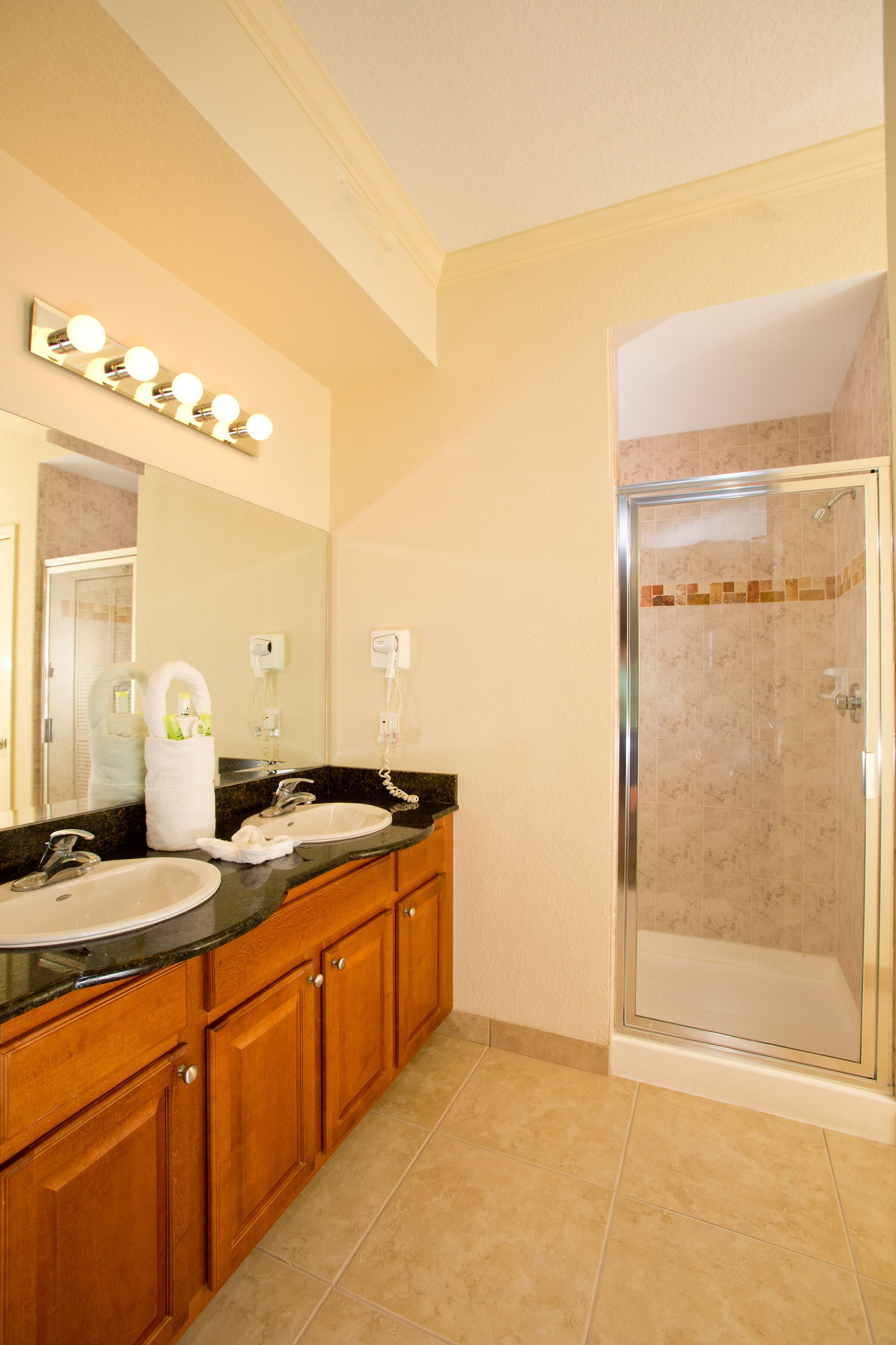 Une salle de bain avec deux lavabos, un miroir et une douche fermée par une paroi de verre.