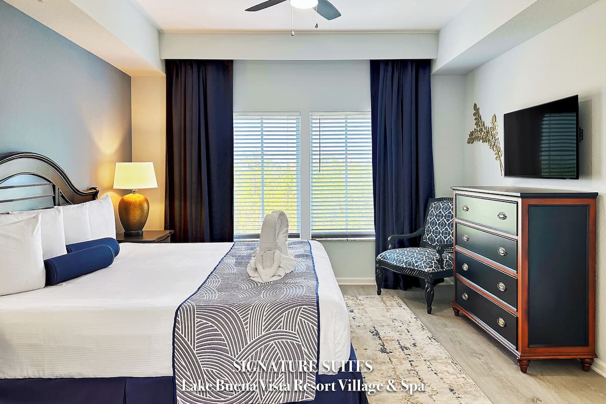 A hotel room with a bed, a dresser, a chair, a television, and a ceiling fan.