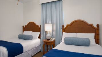 Habitación de hotel con dos camas individuales, una mesita de noche con lámpara y teléfono.