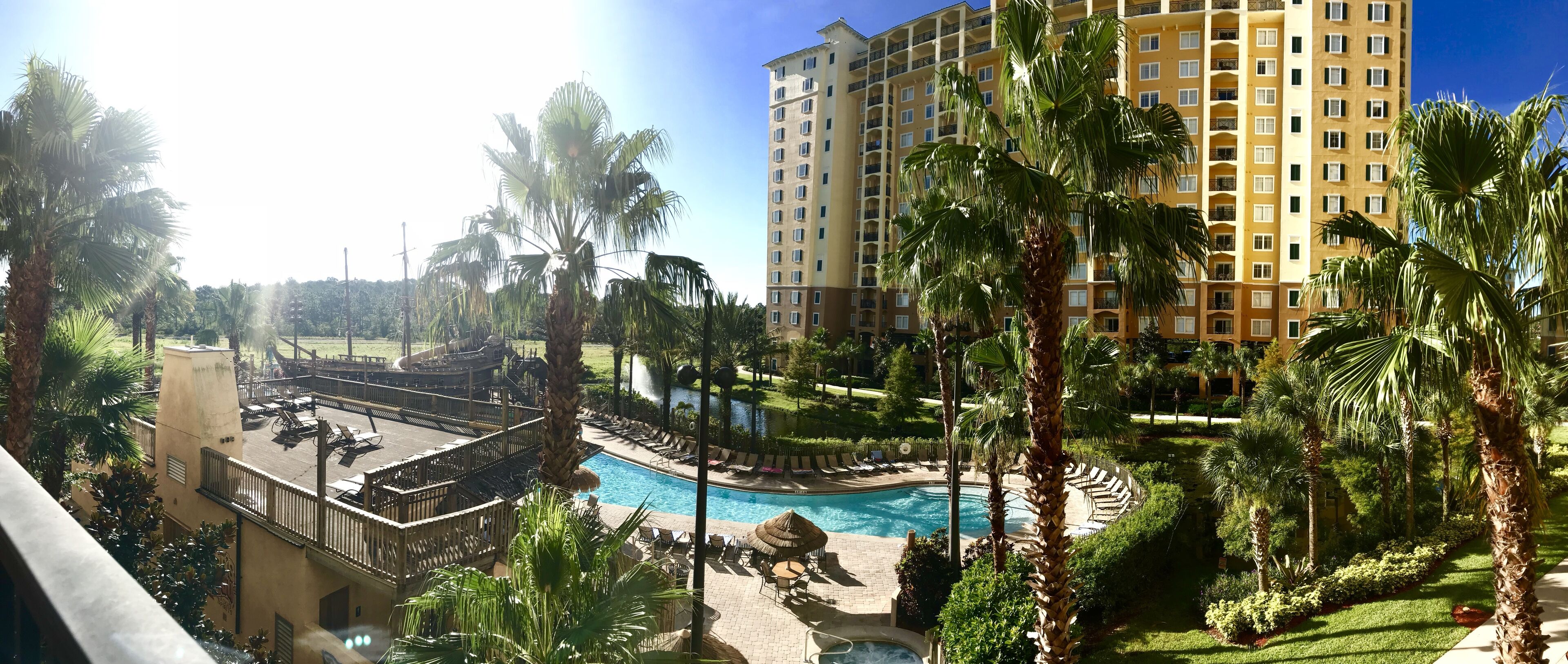 A resort with a swimming pool, palm trees, and a high-rise building in the background.