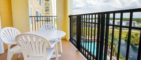 A balcony with a table and chairs, overlooking a swimming pool and buildings.