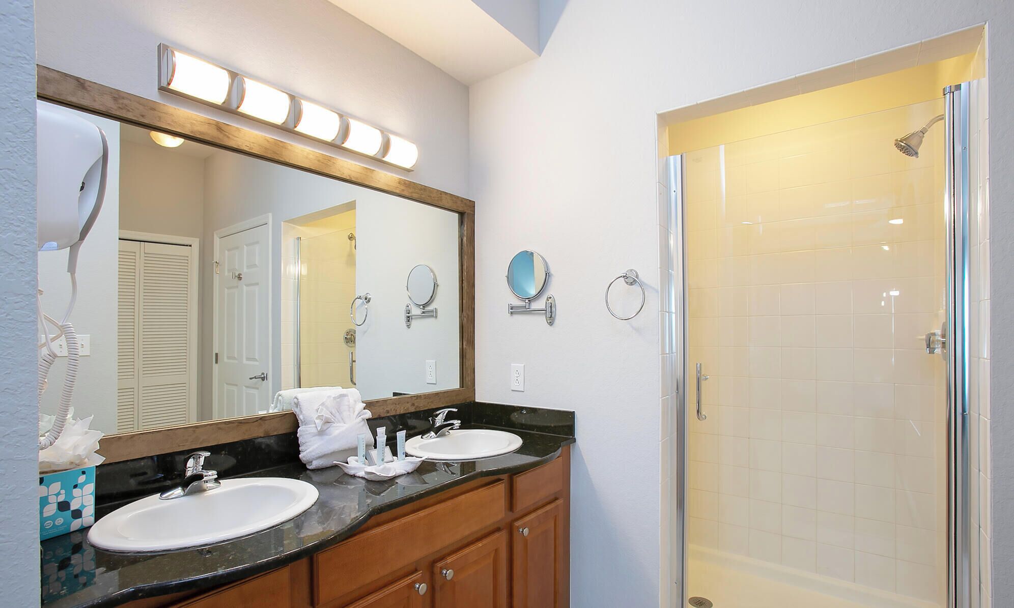 A bathroom with a double sink, a large mirror, a shower, and a towel rack.