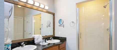 A bathroom with a double sink, a large mirror, a shower, and a towel rack.