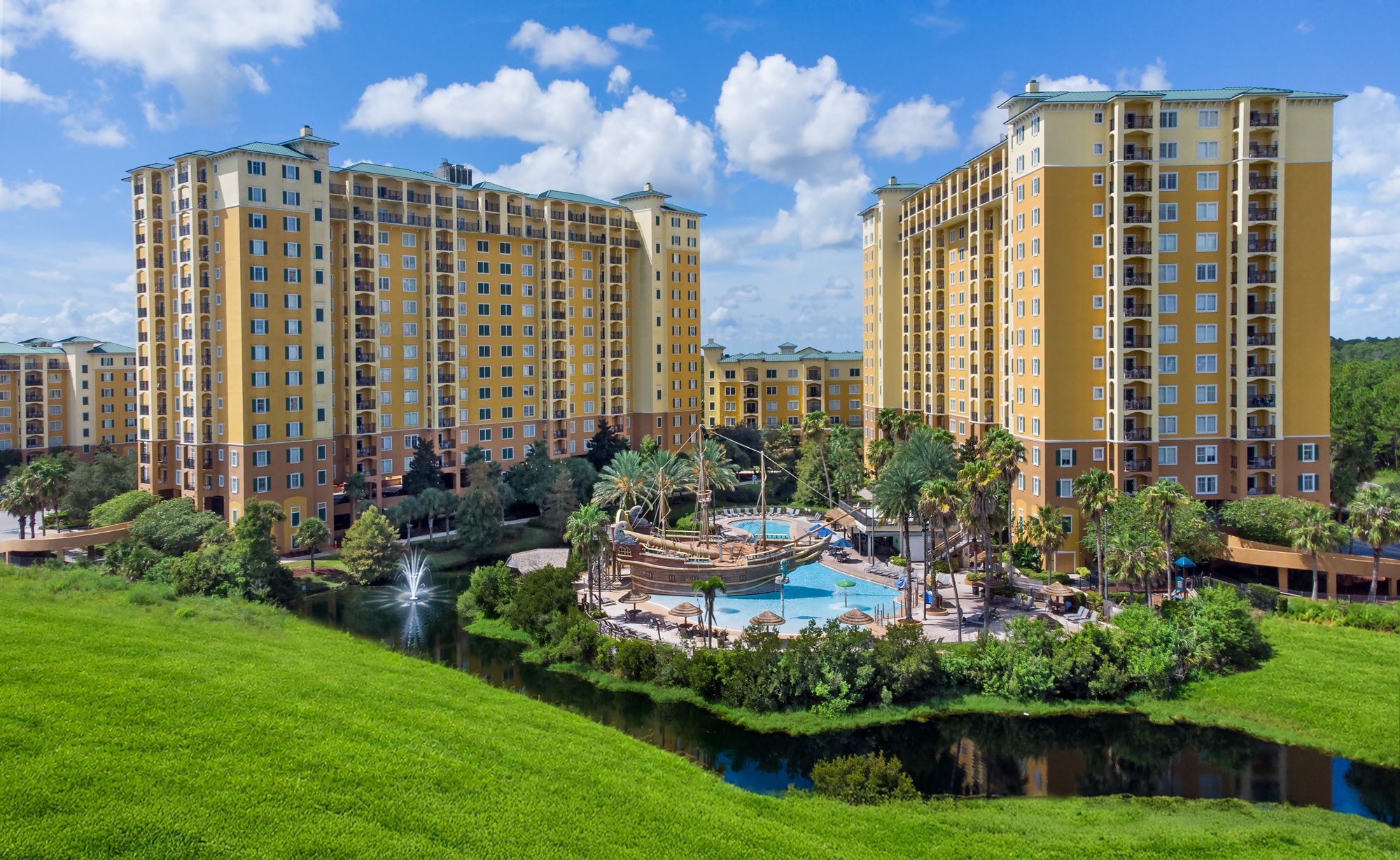 A hotel complex with multiple high-rise buildings, a central swimming pool, and surrounding greenery.