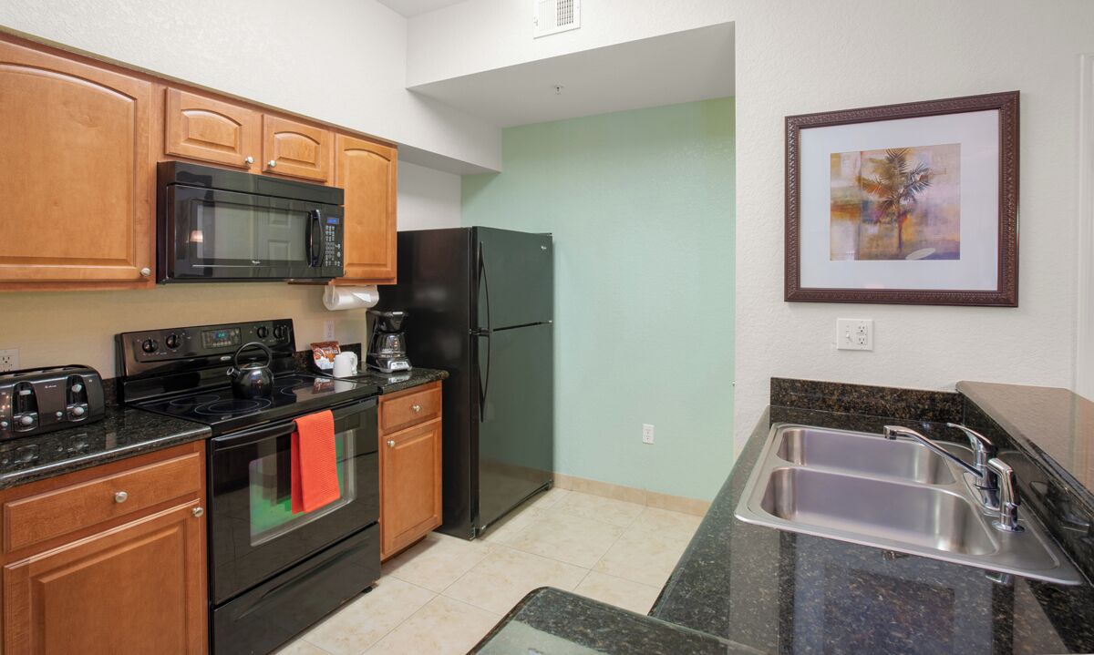 A kitchen with wooden cabinets, a black microwave, a black refrigerator, a stove, and a sink.