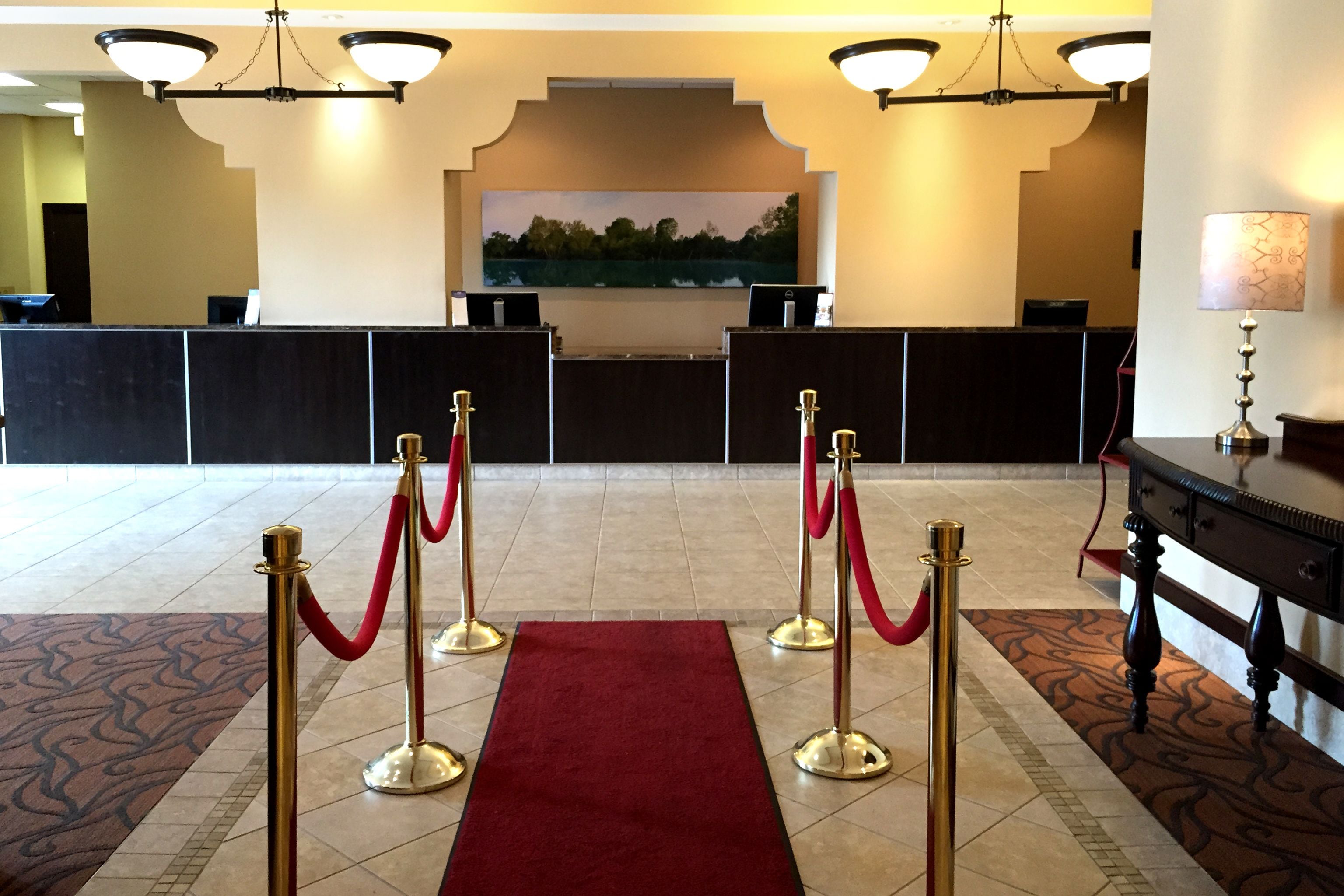 Un espace d’accueil agrémenté d’un tapis rouge, de stanchions dorées et d’un tableau accroché au mur.