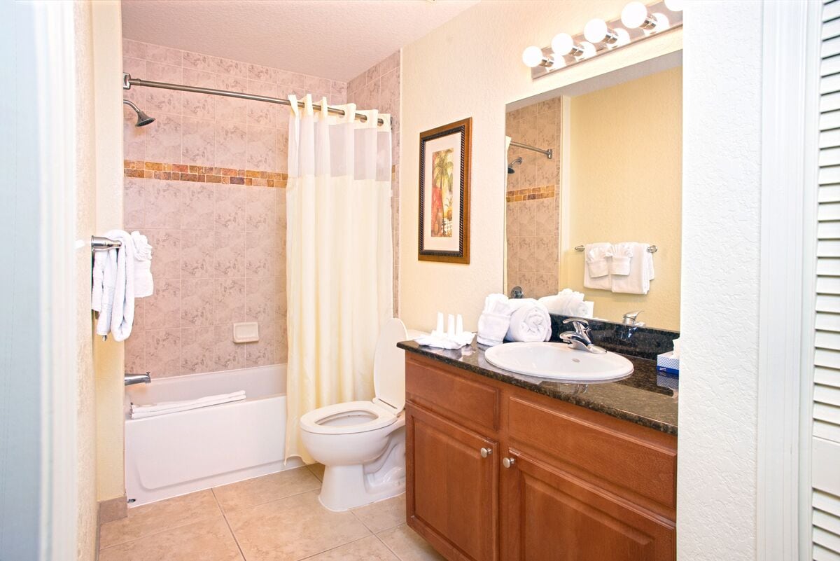 A bathroom with a bathtub, toilet, vanity with a sink, and a mirror.