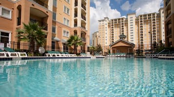 Une piscine entourée de bâtiments à plusieurs étages dotés de balcons, avec des chaises longues et des palmiers.