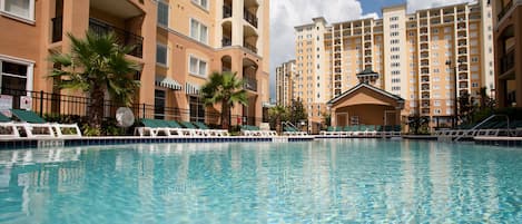 A swimming pool with lounge chairs and palm trees, surrounded by multi-story buildings with balconies.