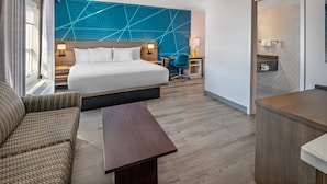 A hotel room with a bed, a desk, a chair, a sofa, and a bathroom visible through an open door.