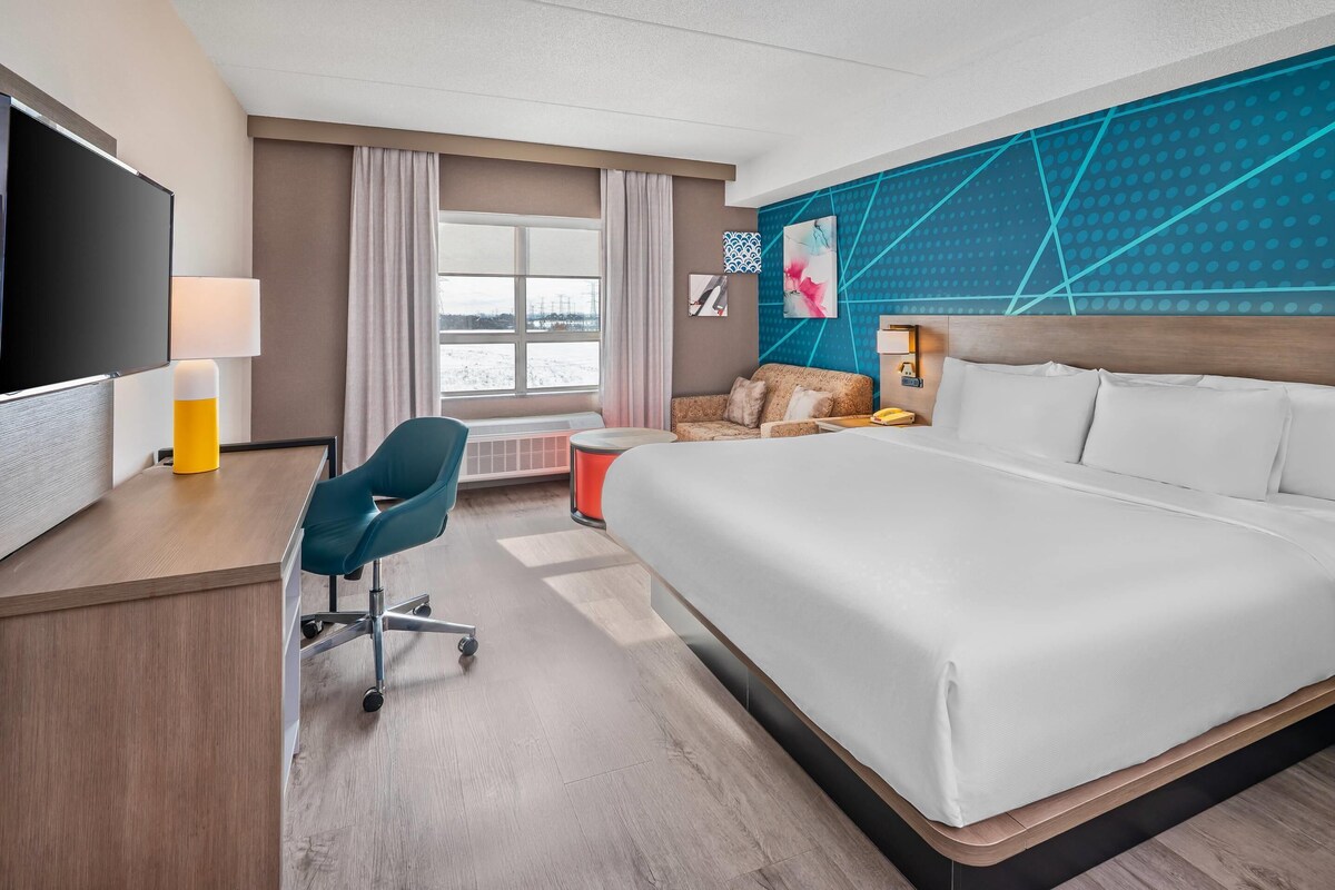 A hotel room with a bed, desk, chair, TV, and a view of the outdoors.