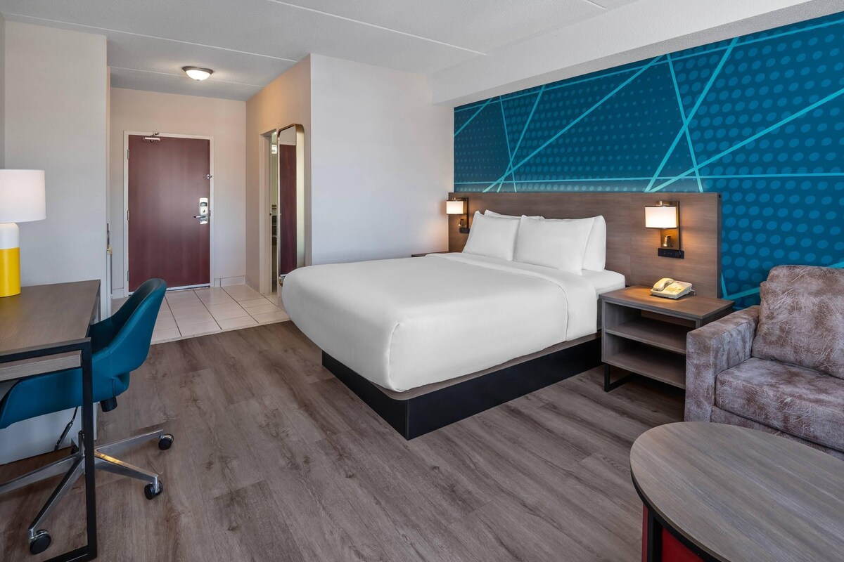 A hotel room with a bed, desk, chair, and a wall with geometric patterns.