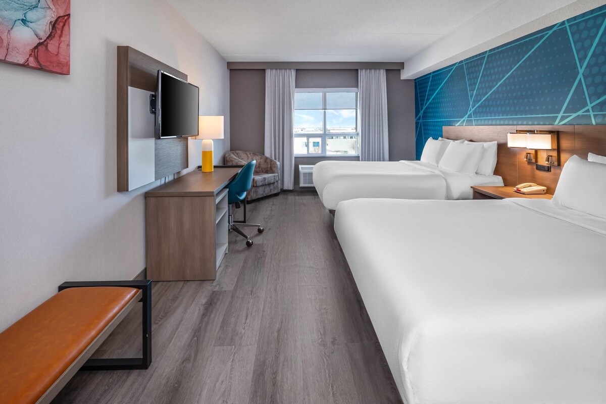 A hotel room with a bed, a desk, a chair, a TV, and a window with curtains.