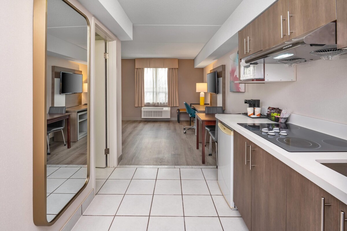 A compact hotel room with a kitchenette, a TV, a desk, and a chair.