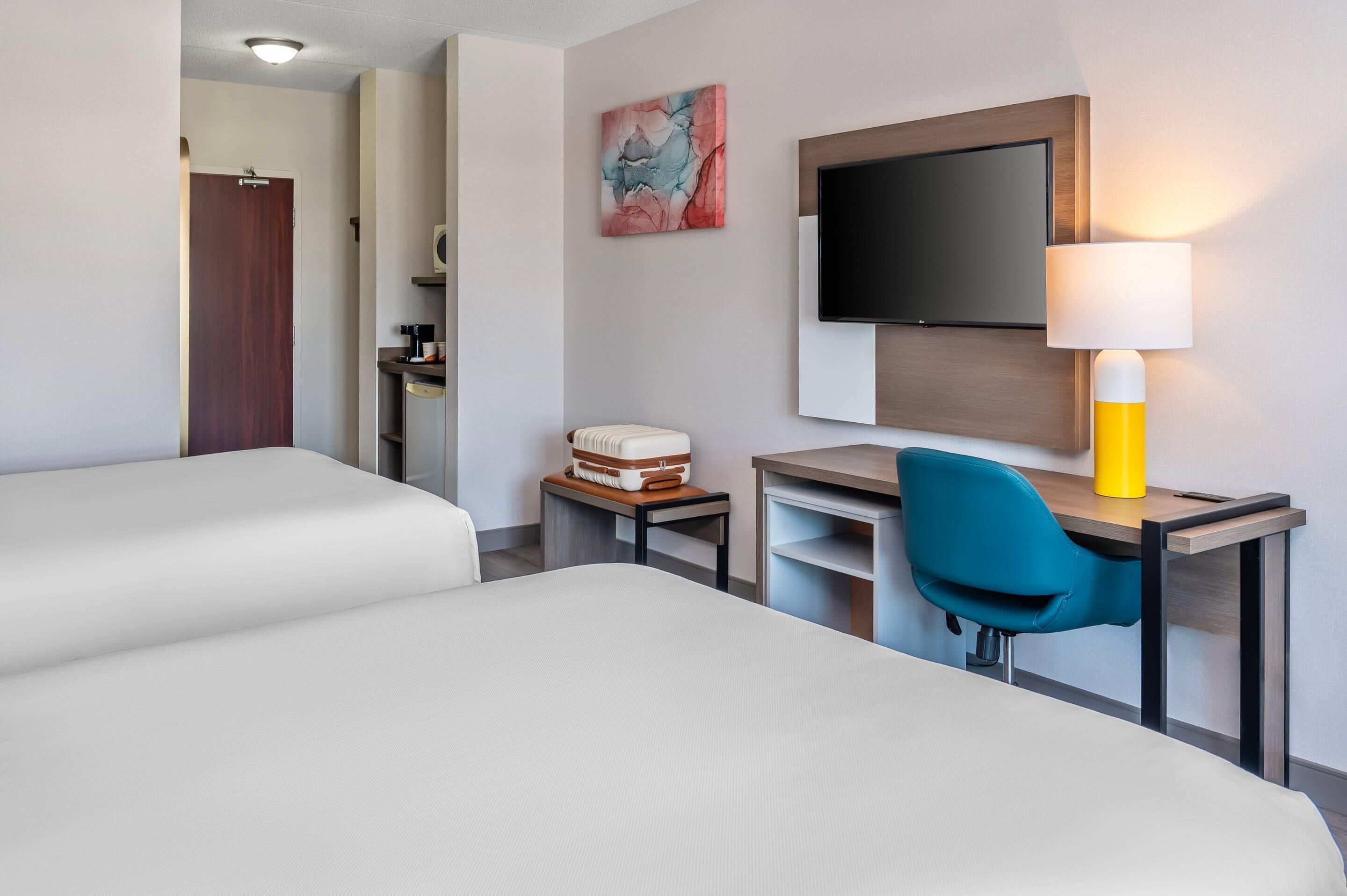 A hotel room with two beds, a desk with a chair, a television, and a lamp.