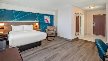 A hotel room with a bed, bedside tables, a chair, a desk, a mirror, and a door.