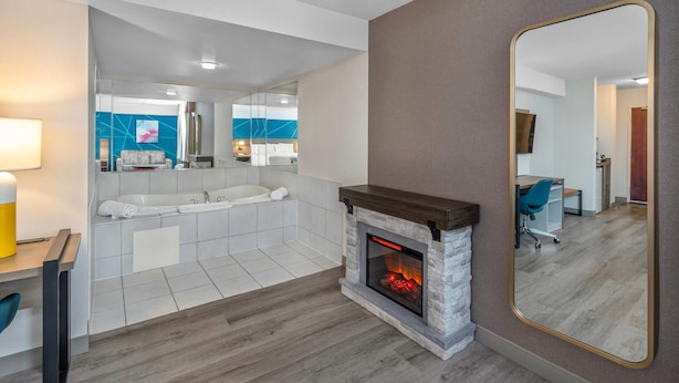 A modern bathroom with a large mirror, a fireplace, and a view into the living area.