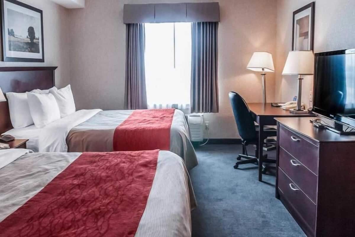 Habitación de hotel con dos camas, un escritorio, una silla, un televisor y una ventana con cortinas.
