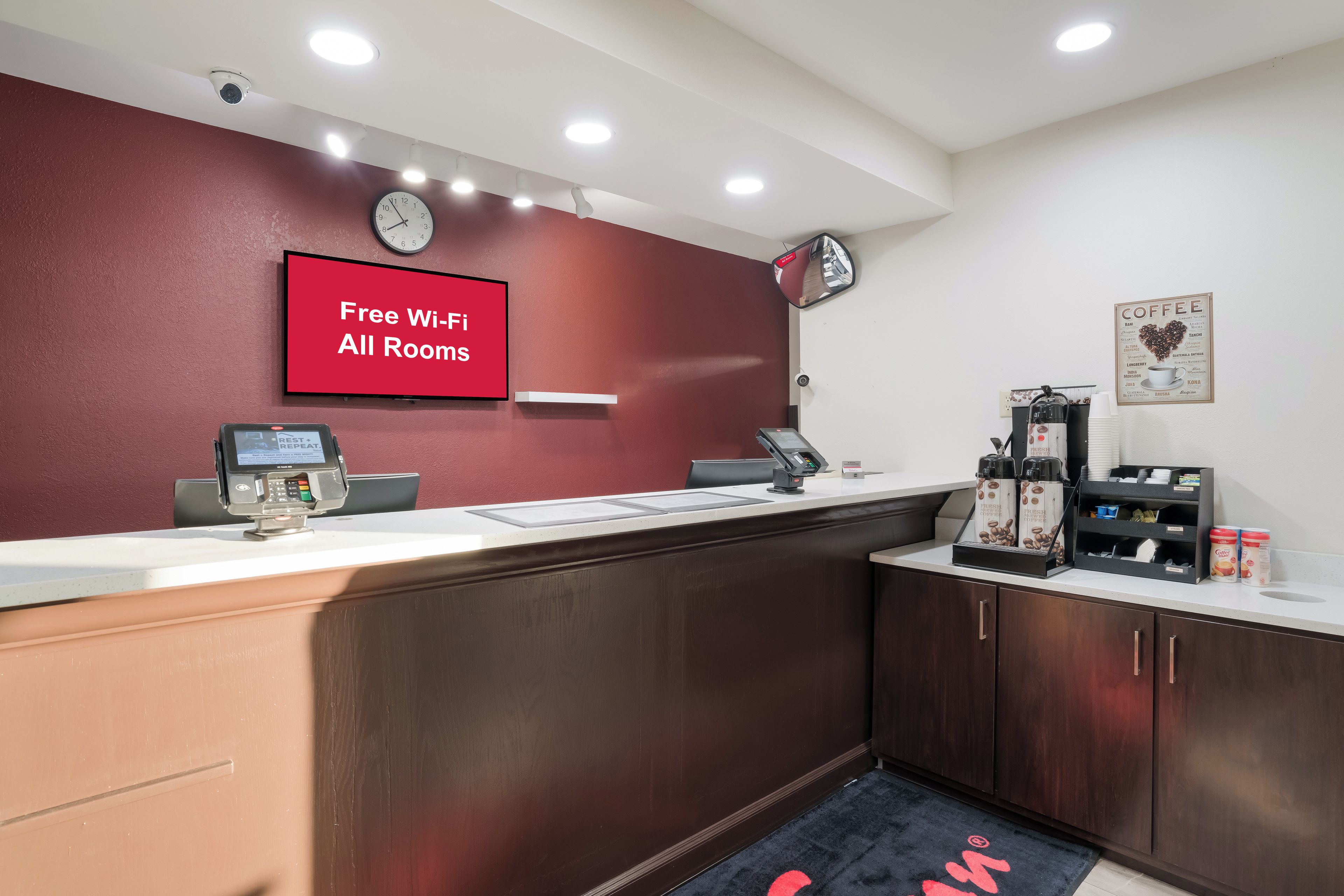 Mostrador de recepción con pantalla digital, un reloj y un cartel que indica acceso a Wi-Fi gratuito.