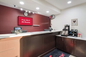 A reception desk with a digital screen, a clock, and a sign indicating free Wi-Fi availability. - Red Roof Inn & Suites Carrollton, GA–West Georgia (Carrollton)