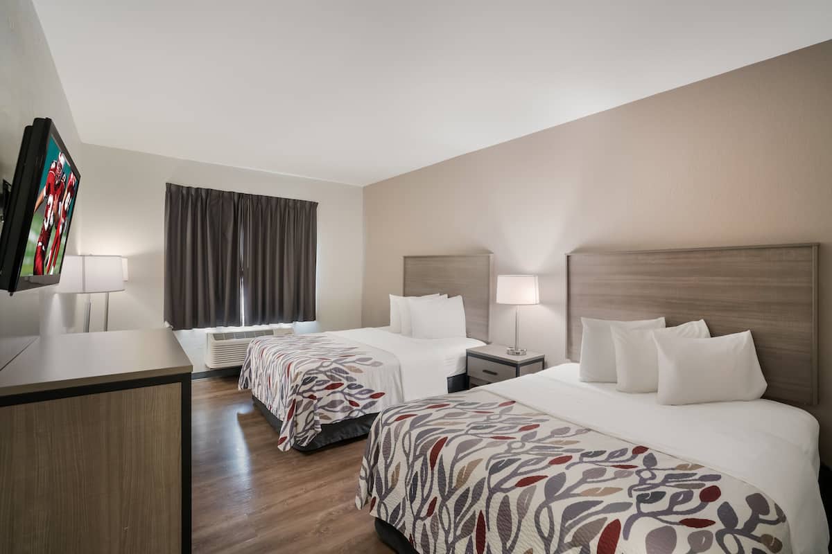 A hotel room with two beds, a desk, a TV, and a window with curtains.